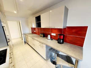 Une cuisine moderne avec des meubles blancs, un pare-feu rouge et une machine à café intégrée.