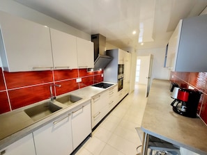Una cocina moderna con armarios blancos, un lavamanos de acero inoxidable, un salpicadero rojo y una cafetera.