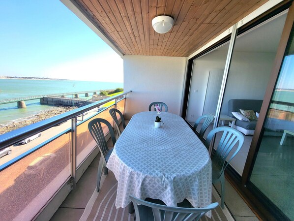 Un balcón con una mesa, sillas, una planta en maceta y vistas al mar.