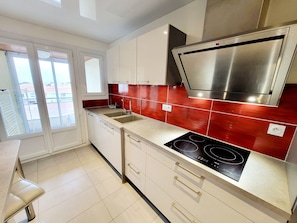 A modern kitchen with a stainless steel range hood, a double sink, and a dishwasher. - 3-room apartment with terrace, garage - La Chaume (Les Sables-d'Olonne)