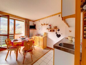 Ein gemütlicher Essbereich mit Holztisch und -stühlen, eine Küche mit Spüle und Herd sowie ein schöner Ausblick durch die Fenster.