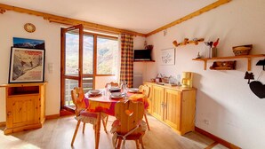 A cozy dining area with a wooden table, chairs, and a view of the mountains through large windows. - Functional studio at the foot of the slopes with balcony (Les Menuires)