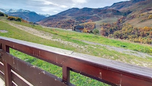 A scenic view of a mountainous landscape with a wooden fence in the foreground, a small building with a dark roof, and autumn-colored trees in the valley. - Functional studio at the foot of the slopes with balcony (Les Menuires)