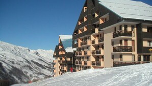 A multi-story hotel with a modern architectural design, featuring balconies and a snow-covered landscape in the background. - Functional studio at the foot of the slopes with balcony (Les Menuires)