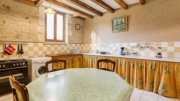 A kitchen with a dining table, wooden beams, a washing machine, and a window.