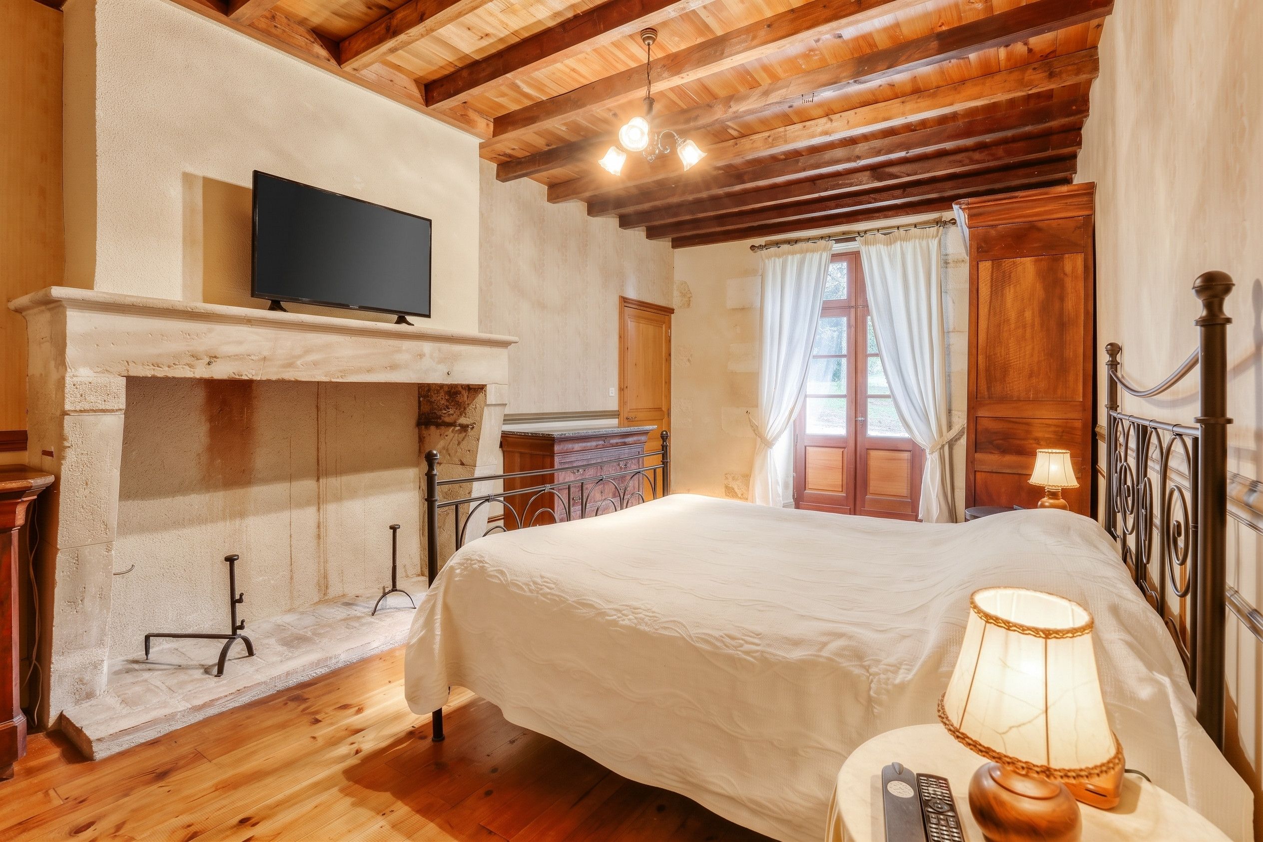 Une chambre à coucher avec un lit, un téléviseur fixé au mur, une cheminée et une fenêtre avec des rideaux.