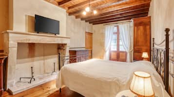 Une chambre à coucher avec un lit, un téléviseur fixé au mur, une cheminée et une fenêtre avec des rideaux.