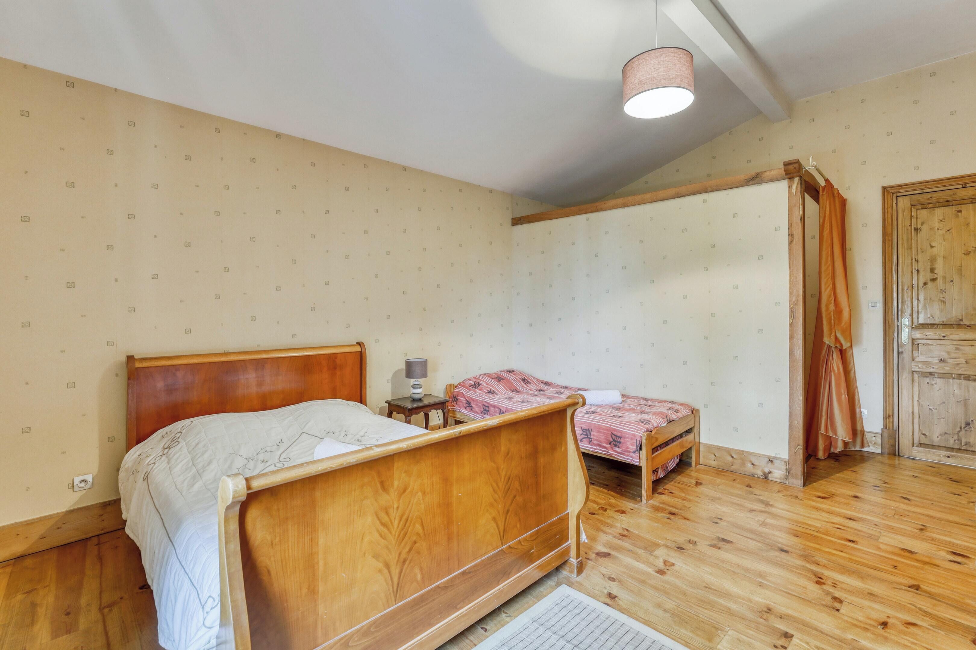 Um quarto com uma cama de madeira, uma cama menor, uma mesinha de cabeceira, um abajur e um guarda-roupa de madeira.