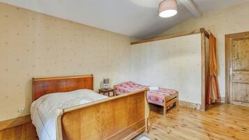 Um quarto com uma cama de madeira, uma cama menor, uma mesinha de cabeceira, um abajur e um guarda-roupa de madeira.