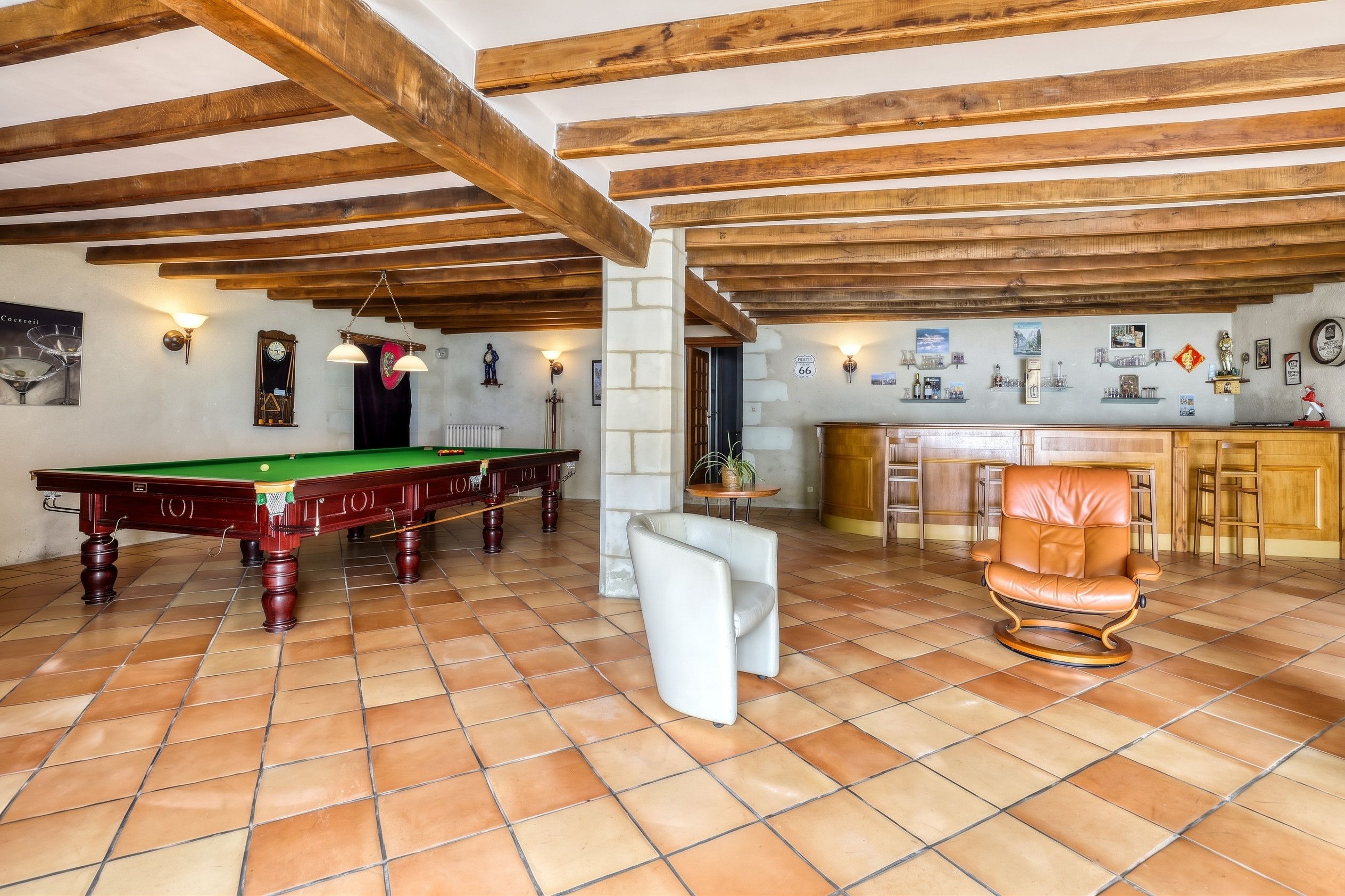 A billiards room with a pool table, a bar area, and a seating area with a chair.