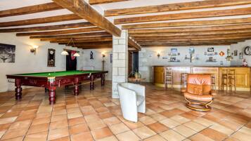 A billiards room with a pool table, a bar area, and a seating area with a chair.