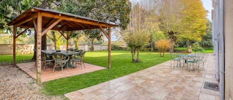 Een terras met een pergola, buitenmeubels en een verzorgd gazon.