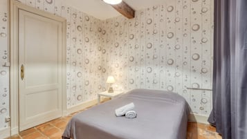 A bedroom with a bed, a nightstand, a lamp, a door, and patterned wallpaper.