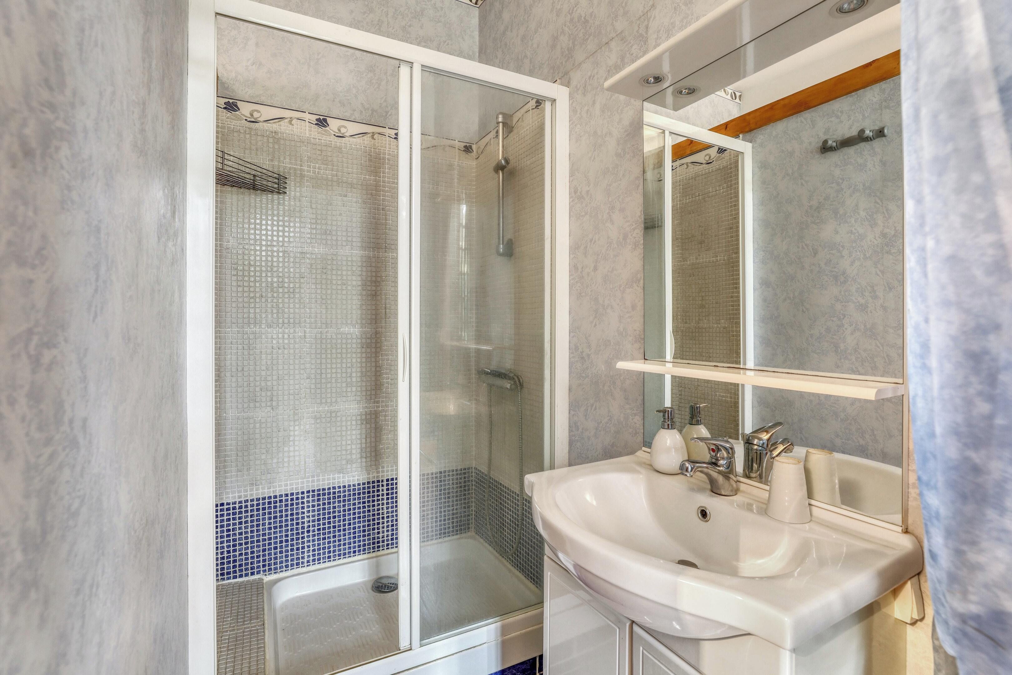 Un baño moderno con ducha envuelta en vidrio, un lavabo blanco y un espejo encima.