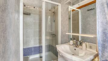 Un baño moderno con ducha envuelta en vidrio, un lavabo blanco y un espejo encima.