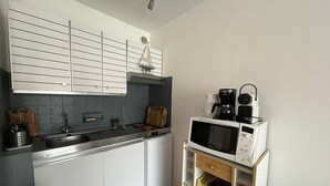 Une cuisine compacte avec des meubles blancs, un four à micro-ondes, une machine à café et un petit évier.