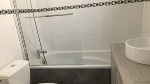 Une salle de bain comprenant des toilettes, une douche à parois de verre et une baignoire.