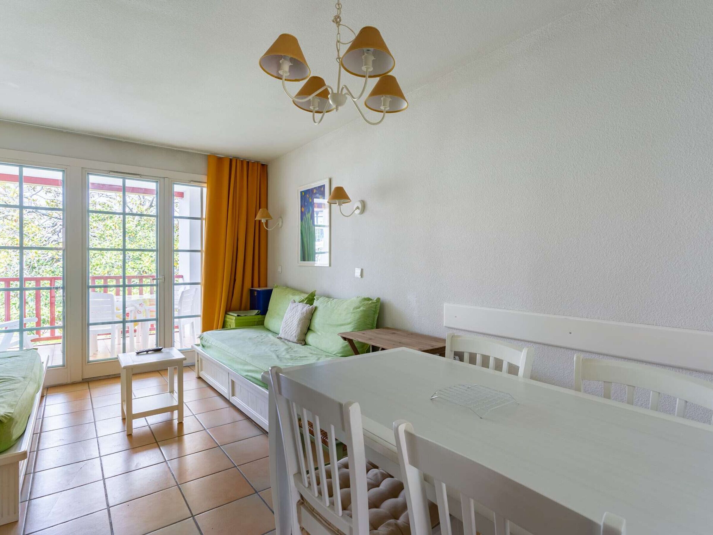 A room with a bed, a dining table, chairs, a bench, a window with curtains, and a ceiling light fixture.