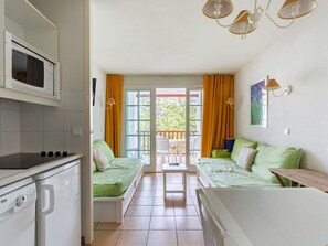 A compact kitchen with a microwave, a stove, and a washing machine. There are two green beds with pillows and a wooden table.