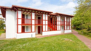 A two-story building with a red and white exterior, a central staircase, and a grassy lawn.