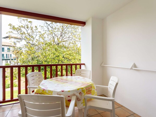 Een balkon met een tafel en stoelen, uitzicht op een boom en een gebouw op de achtergrond.
