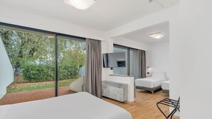A modern hotel room with a large bed, a TV, and a seating area with a view of the garden.