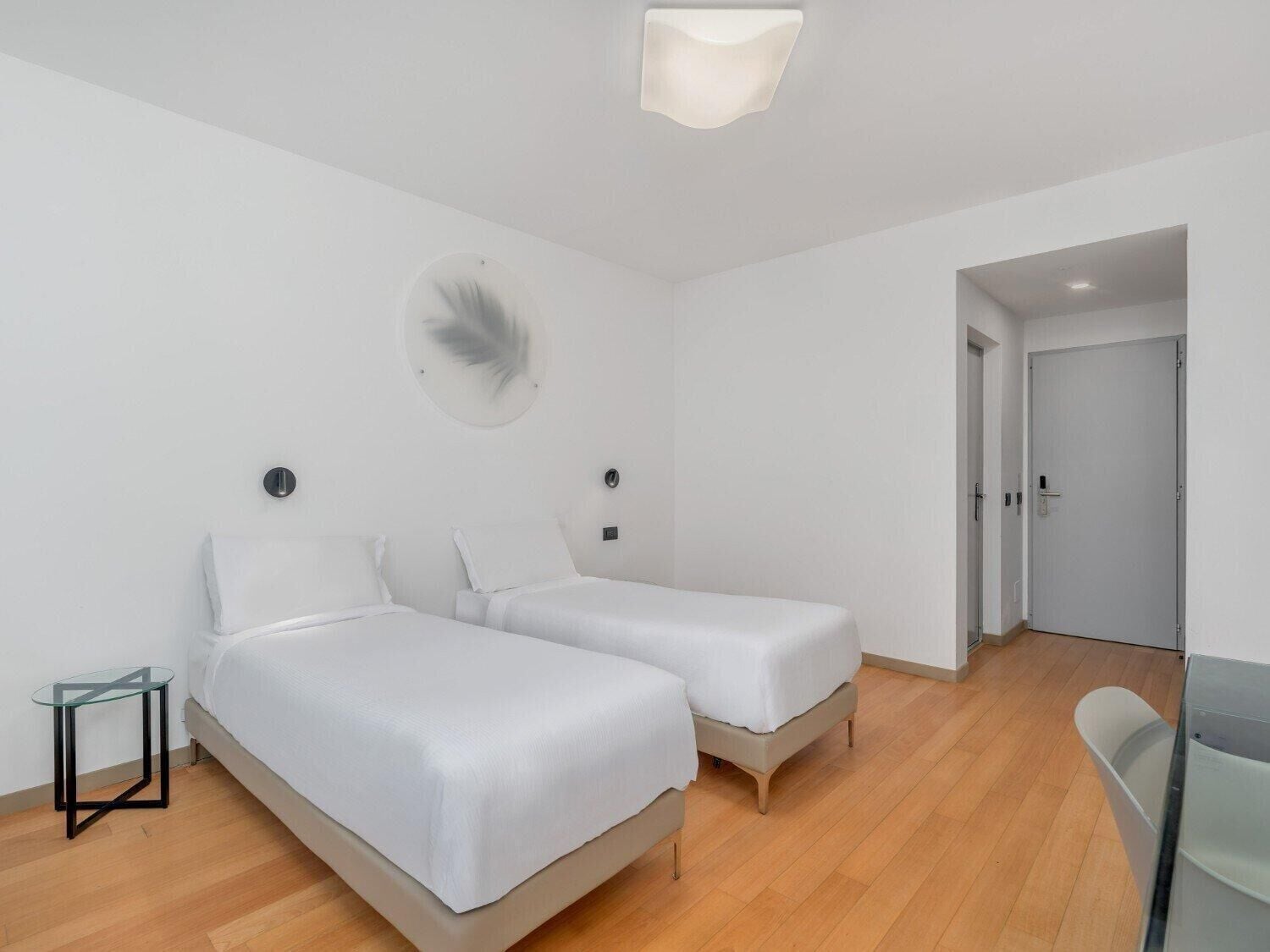 A modern hotel room with two single beds, a glass table, and a round wall decoration.