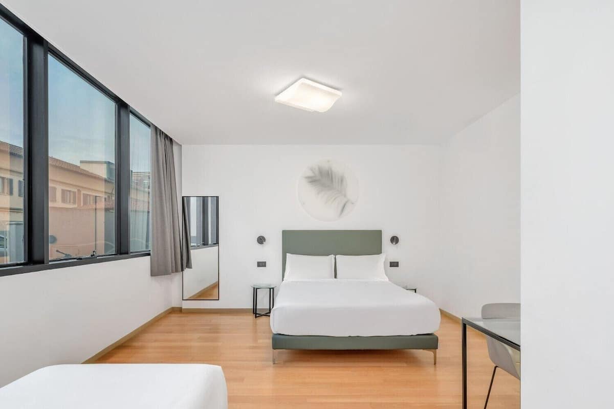 Une chambre d’hôtel moderne dotée d’un grand lit, d’un bureau et offrant une vue sur la ville grâce à de grandes fenêtres.