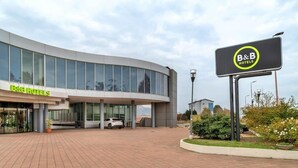 A modern B&B hotel with a large glass facade, a paved entrance, and a signboard. - B&B Hotel Alba (Alba)