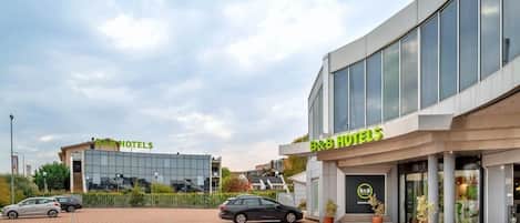 A B&B hotel with a modern glass facade, a parking lot, and a clear sky.