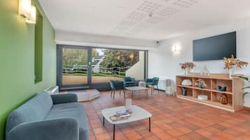 Ein modernes Wohnzimmer mit einem grauen Sofa, einem Couchtisch und stählfarbenen Sesseln. Ein Bücherregal mit Dekorationselementen und ein Flachbildfernseher an der Wand sind ebenfalls vorhanden.