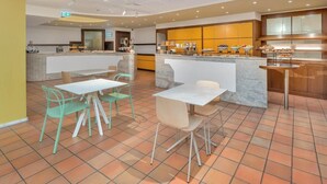A modern kitchen with a central island, a breakfast bar, and a seating area with chairs and tables.