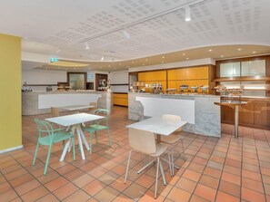 A modern kitchen with a central island, a breakfast bar, and a seating area with chairs and tables.