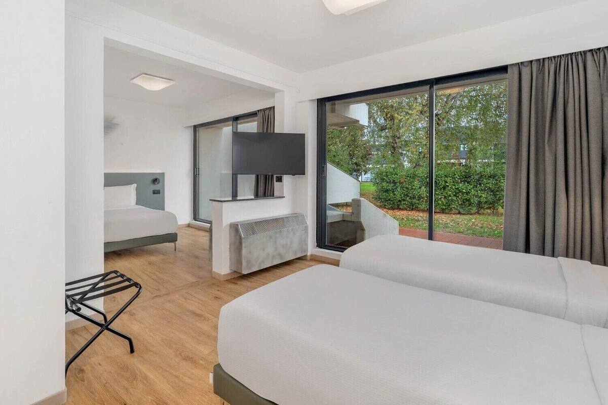 Une chambre d’hôtel moderne avec un grand lit, un téléviseur fixé au mur et une vue sur l’extérieur.