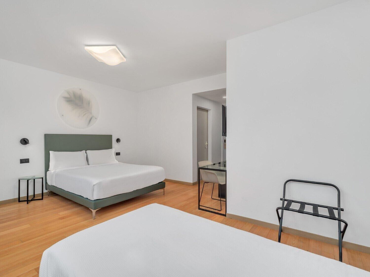 A minimalist hotel room with a single bed, a small table, a chair, and a desk.