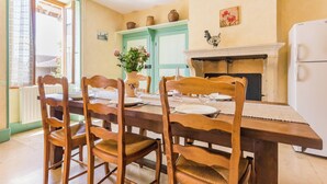 A dining area with a wooden table set for four, surrounded by wooden chairs. A vase of flowers is on the table, and there is a fireplace with a mantel above it. - Homerez - House in Éringes, parking included (Éringes)