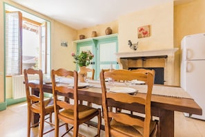 A dining area with a wooden table set for four, surrounded by wooden chairs. A vase of flowers is on the table, and there is a fireplace with a mantel above it. - Homerez - House in Éringes, parking included (Éringes)