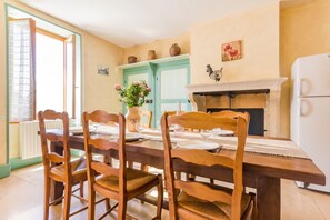 A dining room with a wooden table set for four, chairs, a vase with flowers, a fireplace, and a white refrigerator.