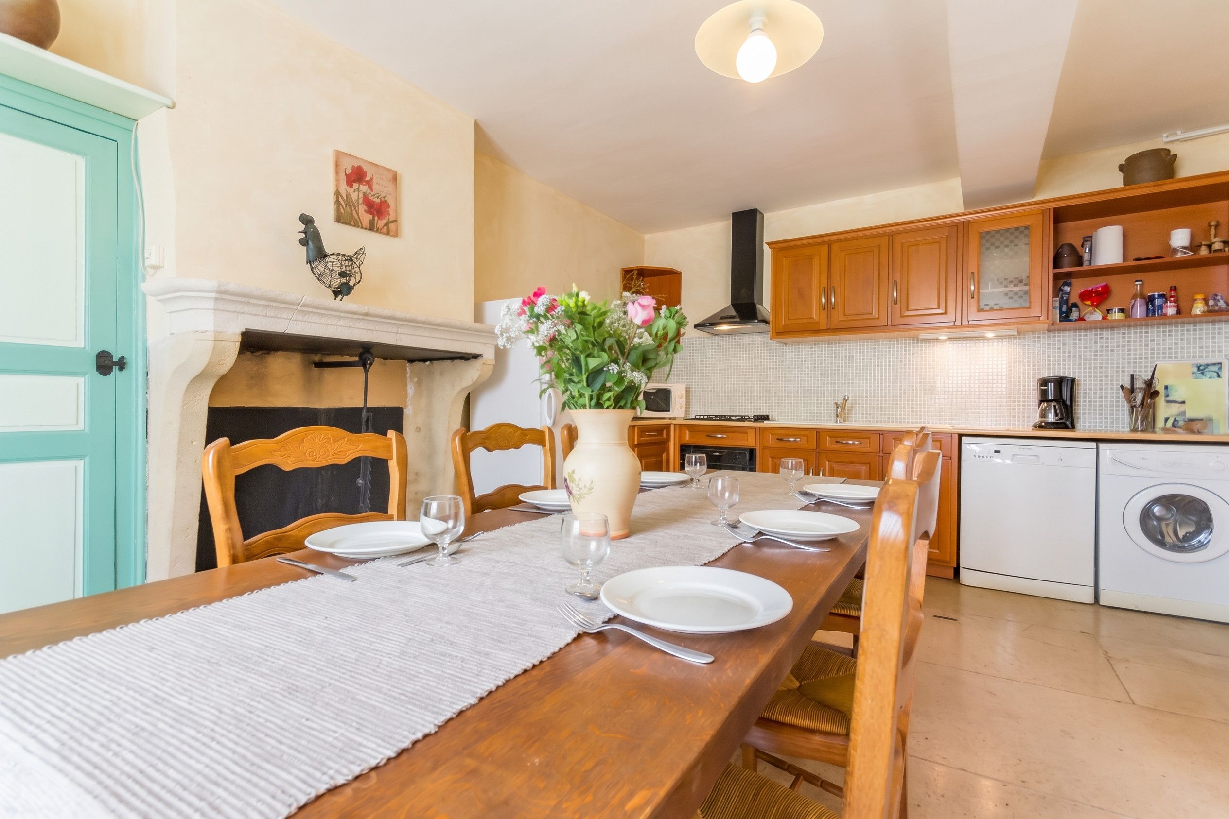 Un coin repas avec une table en bois dressée pour quatre personnes, un vase rempli de fleurs et une cheminée.