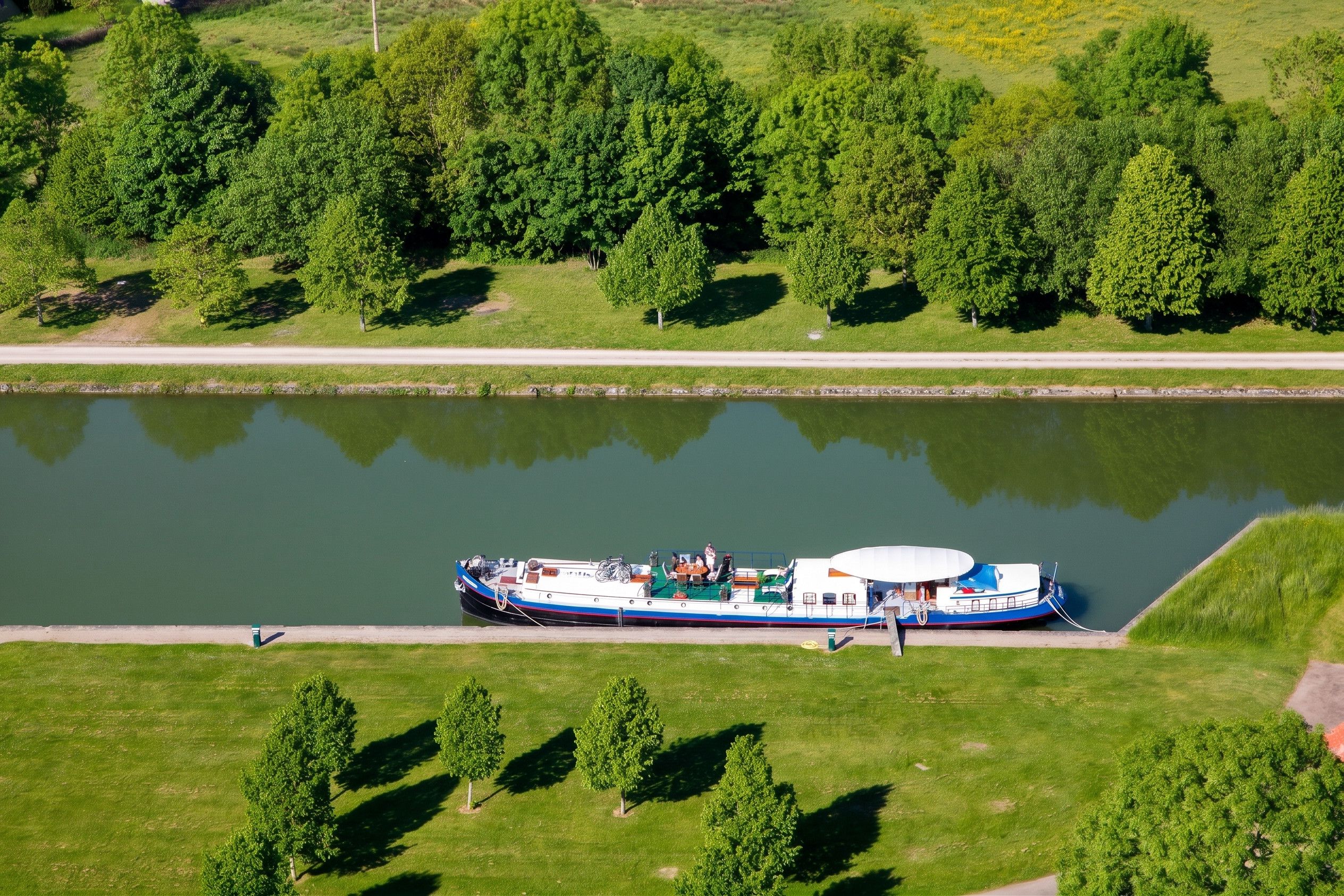 Una nave da fiume ormeggiata lungo la riva di un fiume, con una zona erbosa e alberi sullo sfondo.