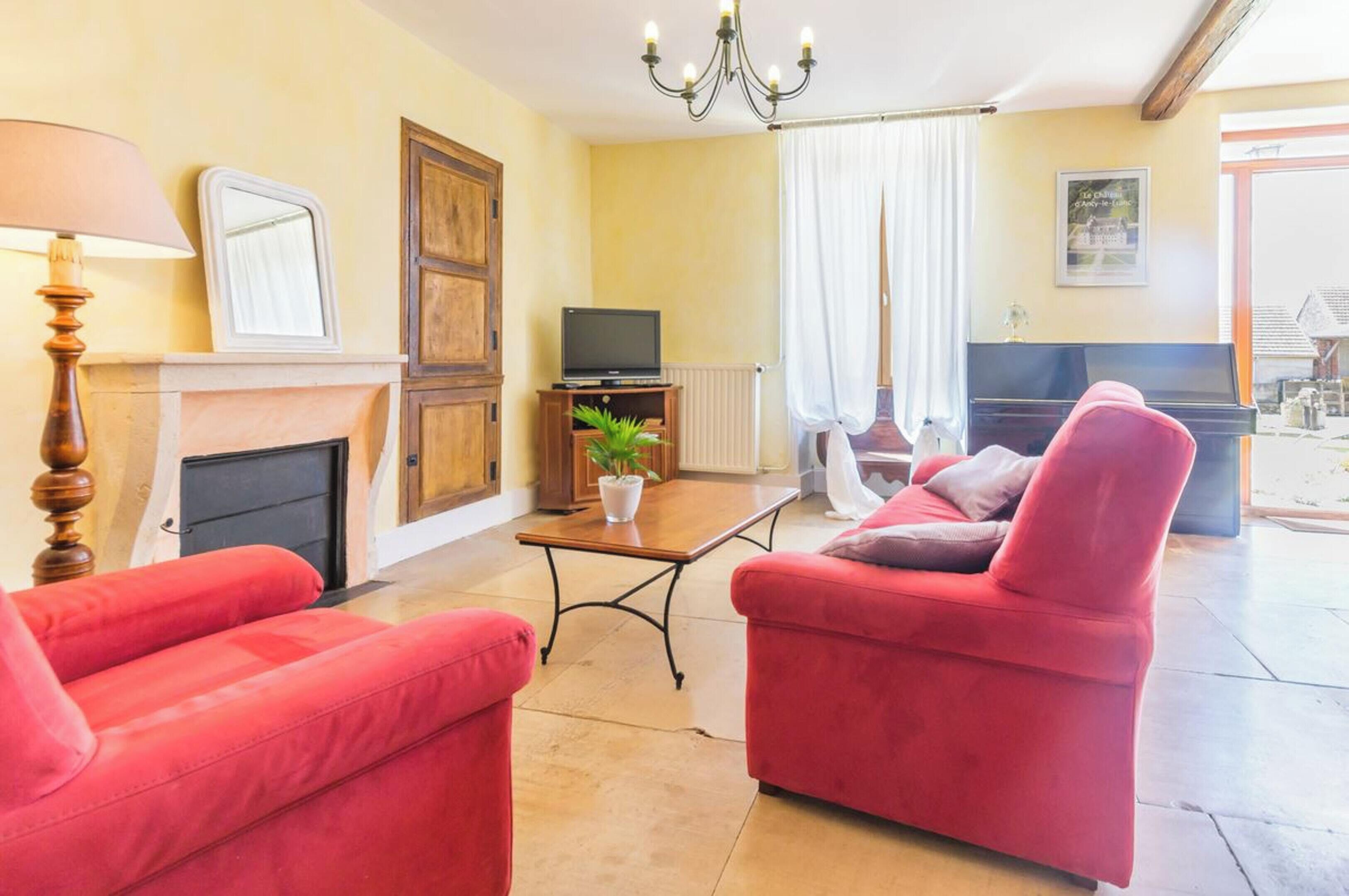 A living room with red sofas, a fireplace, a television, and a piano.