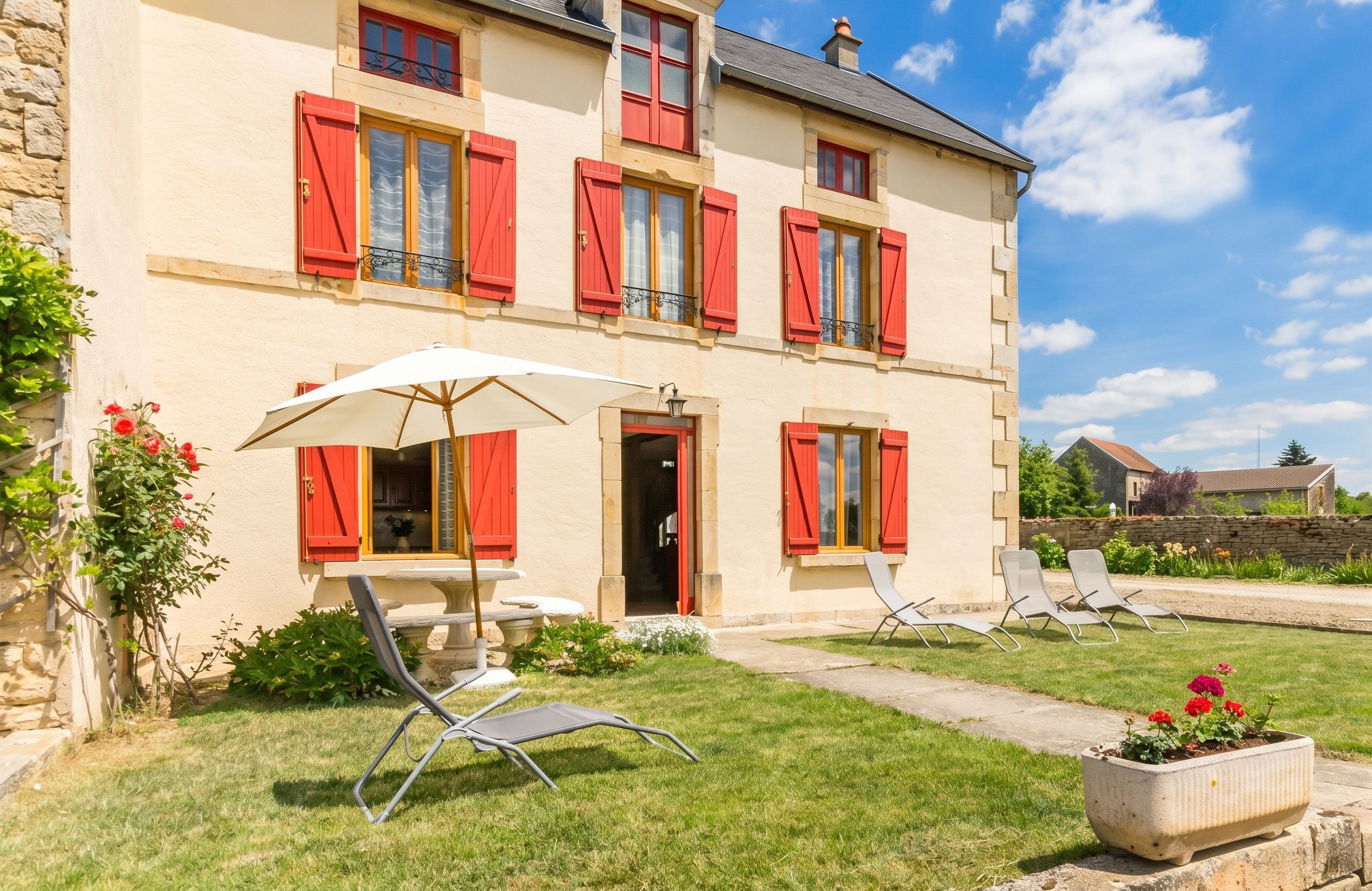 A two-story building with red shutters, a white umbrella, and outdoor seating.