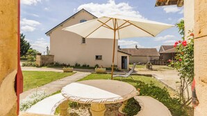 A patio with a table and umbrella, surrounded by a garden and a house. - Homerez - House in Éringes, parking included (Éringes)