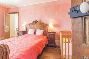 Ein Schlafzimmer mit einem großen Bett, zwei Nachttischen mit Lampen, einem Holckrippenbett und einer Tür.