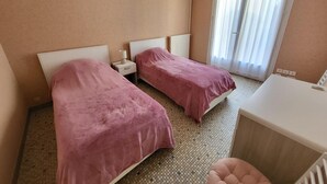 Een hotelkamer met twee bedden, een klein bureau, een stoel en een raam met gordijnen.