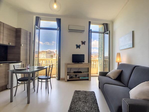 A modern living room with a dining area, a sofa, a TV, and a balcony with a city view.