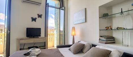 A hotel room with a bed, a television, a desk, a lamp, and a view of the city.