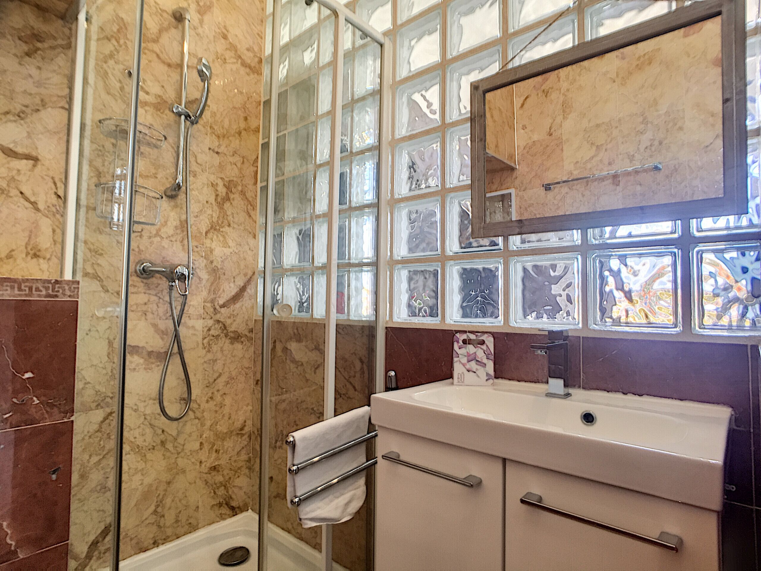 A bathroom with a glass shower enclosure, a marble-tiled wall, a sink with a mirror, and decorative glass panels.