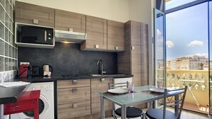 Een moderne keuken met een ingebouwde magnetron, een spoelbak en houten kastjes. Er is een eettafel met twee stoelen en een uitzicht op de stad door grote ramen.