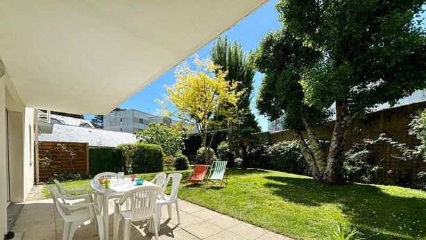 Une terrasse avec une table et des chaises, entourée d’une pelouse bien entretenue et d’arbres.